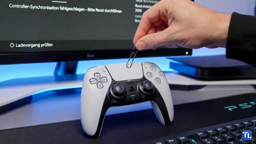 Ein DualSense Controller wird mit einer Büroklammer zurückgesetzt, während ein Monitor deutsche Hilfe-Anweisungen zeigt.