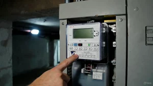 Digitaler Stromzähler im Sicherungskasten, Finger zeigt auf den Namen des Netzbetreibers.